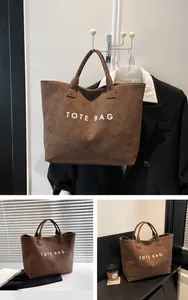Λεπτομέρεια καφέ σουέτ τσάντας tote με μεγάλη χωρητικότητα και λευκά τυπωμένα γράμματα