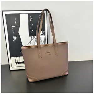 Close-up of brown pebble grain leather tote with minimalist metallic brand plaque