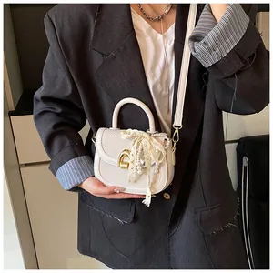 Détail du sac selle blanc avec nœud en dentelle, perles et pendentif cœur doré