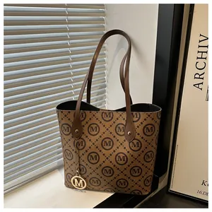 Detalle de bolso tote marrón con estampado de letras M y colgante dorado en ventana