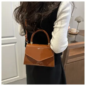 Sac à main en cuir verni marron porté par un mannequin, forme trapèze et détails dorés