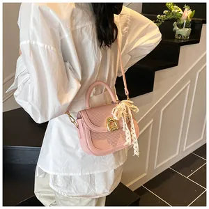 Détail du sac selle rose clair avec texture tissée, fermoir doré et breloque en dentelle