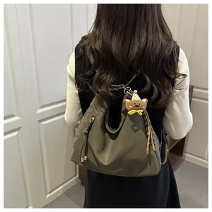 Detail of olive green tote bag featuring side zipper, tassels and brown bear pendant