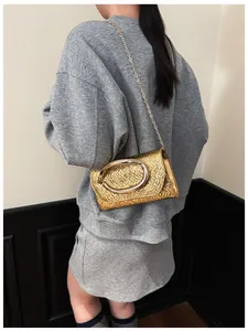 Detail of a metallic gold square crossbody bag with textured finish and oval metal buckle