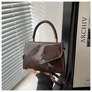 Détail d'un sac à main marron foncé en cuir verni brillant avec rabat et boucles dorées