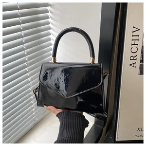 Détail d'un sac à main en cuir verni noir brillant avec finitions dorées et rabat chic