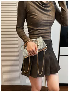 Detail of silver textured crossbody bag with gold round handle and chain strap on a model