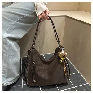 Detail of dark brown tote bag featuring suede texture and decorative bear keychain charm