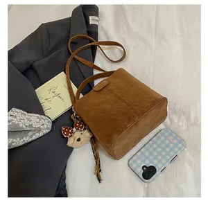Details einer braunen Wildleder-Eimertasche im Vintage-Stil mit Plüschbären-Anhänger