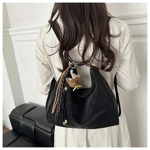 Detail of black leather underarm bag with woven tassel and brown plush bear charm