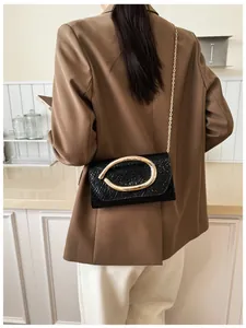Detail of black textured flap bag with large gold oval buckle and elegant gold chain strap