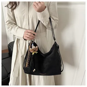Detail of black leather shoulder bag with gold text, bear charm and stripe tassel