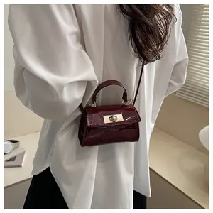 Detail of burgundy patent leather handbag featuring a golden swivel lock and glossy finish