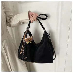 Detail of black tote bag featuring a cute bear charm and golden logo on soft leather