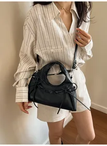 Detail of a black matte tote bag with pleated handles and decorative ribbons on shoulder