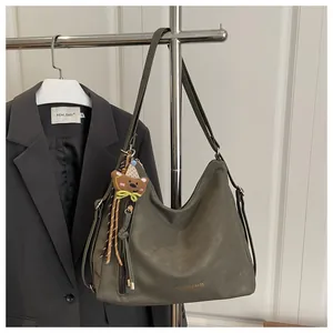 Detail of dark olive green leather tote bag with a cute bear pendant and golden text