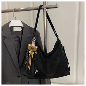 Detail of black suede hobo bag with fringe zipper, bear charm and printed text logo