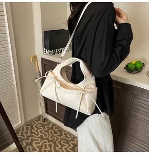 Chic cream bow shoulder bag with pleated detail shown on a model in a cozy setting