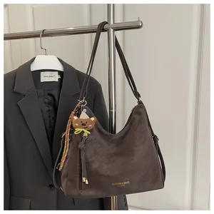 Detailed view of brown tote bag with bear charm hanging on a silver metal coat hanger