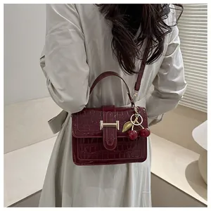 Détail du sac à main bordeaux à motif crocodile avec breloque cerise et boucle dorée