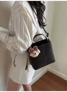 Detail of dark brown bucket bag with plush bear charm and decorative dotted silk scarf