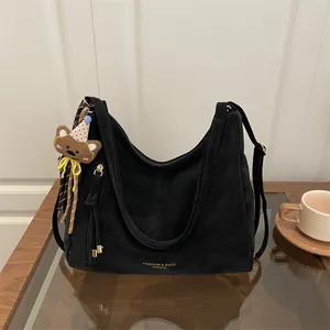Minimalist black hobo shoulder bag with bear pendant on a table with a coffee cup