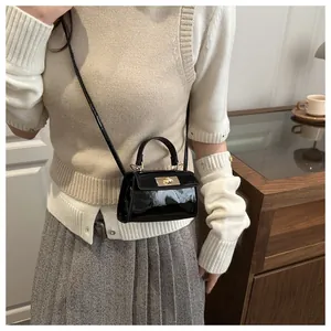 Detail of a mini black patent leather handbag with metal twist lock and thin shoulder strap