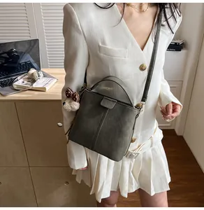 Dark green suede bucket bag with bear pendant shown on model in a modern home interior