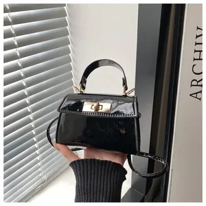 Detailed view of black patent leather mini handbag with gold metal twist lock and handle