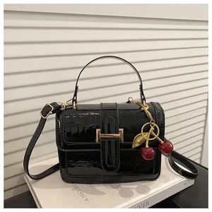 Détail d'un sac à main noir motif crocodile avec breloque cerise et fermoir doré chic
