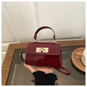 Detail of burgundy glossy mini handbag with a golden metal twist-lock and slim shoulder strap