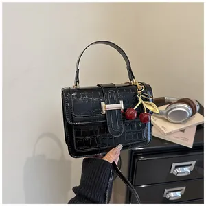 Détail du sac à main noir motif crocodile avec breloque cerise et fermoir doré chic
