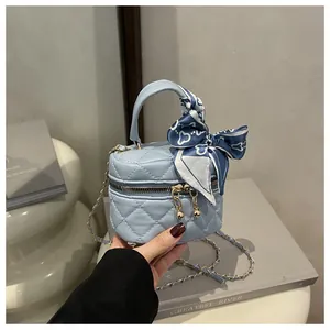 Detail of light blue quilted mini bag featuring a golden ball zipper and silk scarf handle