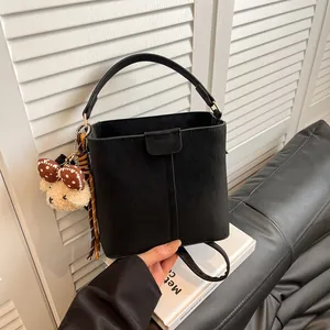 Retro black suede bucket bag with plush bear charm shown in a stylish handheld lifestyle view