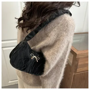 Dettaglio di una borsa a tracolla plissettata nera con fiocco dorato su tessuto opaco