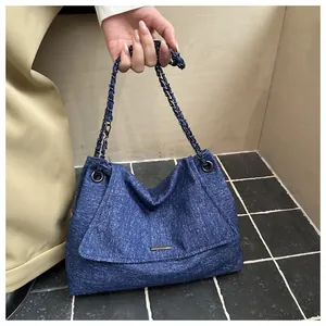 Close-up of blue denim texture tote bag featuring metallic chain strap and magnetic flap