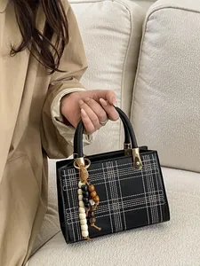Minimalist black plaid tote bag with beaded charm and gold hardware on a beige sofa