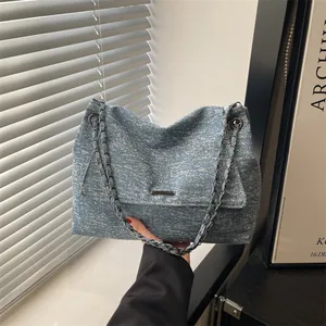 Blue tweed tote bag with metal chain straps and rectangular flap shown in a minimalist room