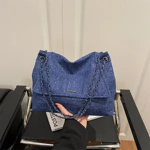 Navy blue denim tote bag with chain strap and silver buckle shown in hand