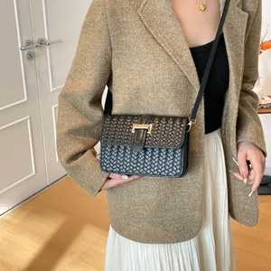 Sac baguette en cuir tressé noir avec boucle dorée en T porté par un mannequin