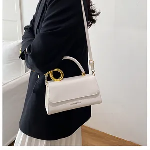 Model wearing a cream white crossbody bag with gold ring handle and metal hardware