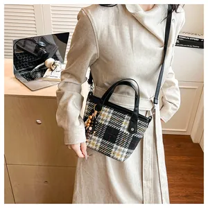 Detail of plaid tote bag with leather handles, wooden bead charm and metal zipper