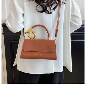 Detailed view of a retro brown leather bag with golden metal handle on a white blazer