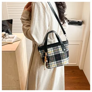 Plaid tote bag with wooden bead tassel and leather strap shown on shoulder