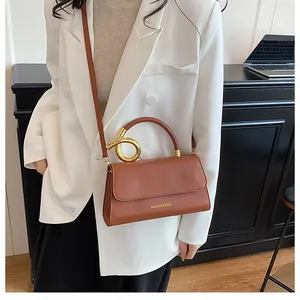 Detail of a brown leather shoulder bag with a gold circular handle and magnetic flap
