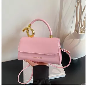 Detail of pink crossbody bag with a modern twisted gold metal handle against white background