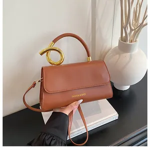 Detail of a brown leather bag featuring a unique twisted gold metal handle and logo
