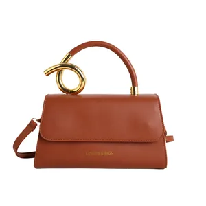 Brown leather crossbody bag with artistic gold metal handle and minimalist fashion design