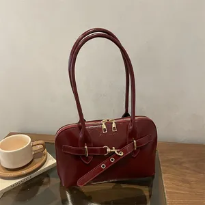 Retro Schultertasche aus weinrotem Lackleder mit goldener Schnalle auf Holztisch