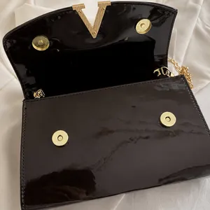 Détail du fermoir doré en V sur le sac à bandoulière en cuir verni marron foncé